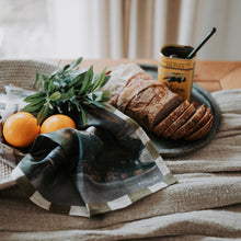 Load image into Gallery viewer, Bread, oranges, and a glass of juice on a wooden table with a checkered cloth.